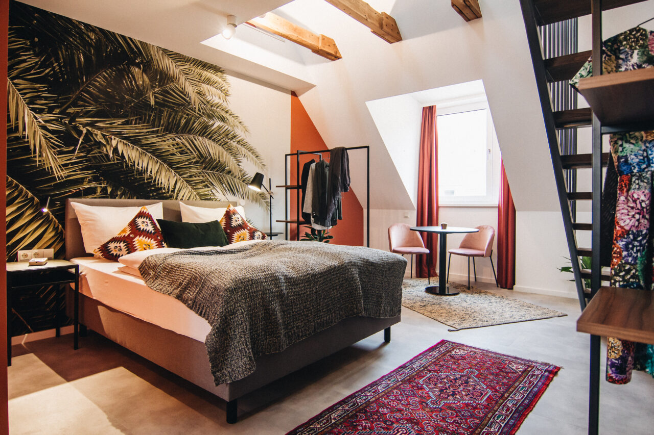 Bett unter der Dachschräge mit Wandbild aus Palmen und sichtbaren Holzbalken