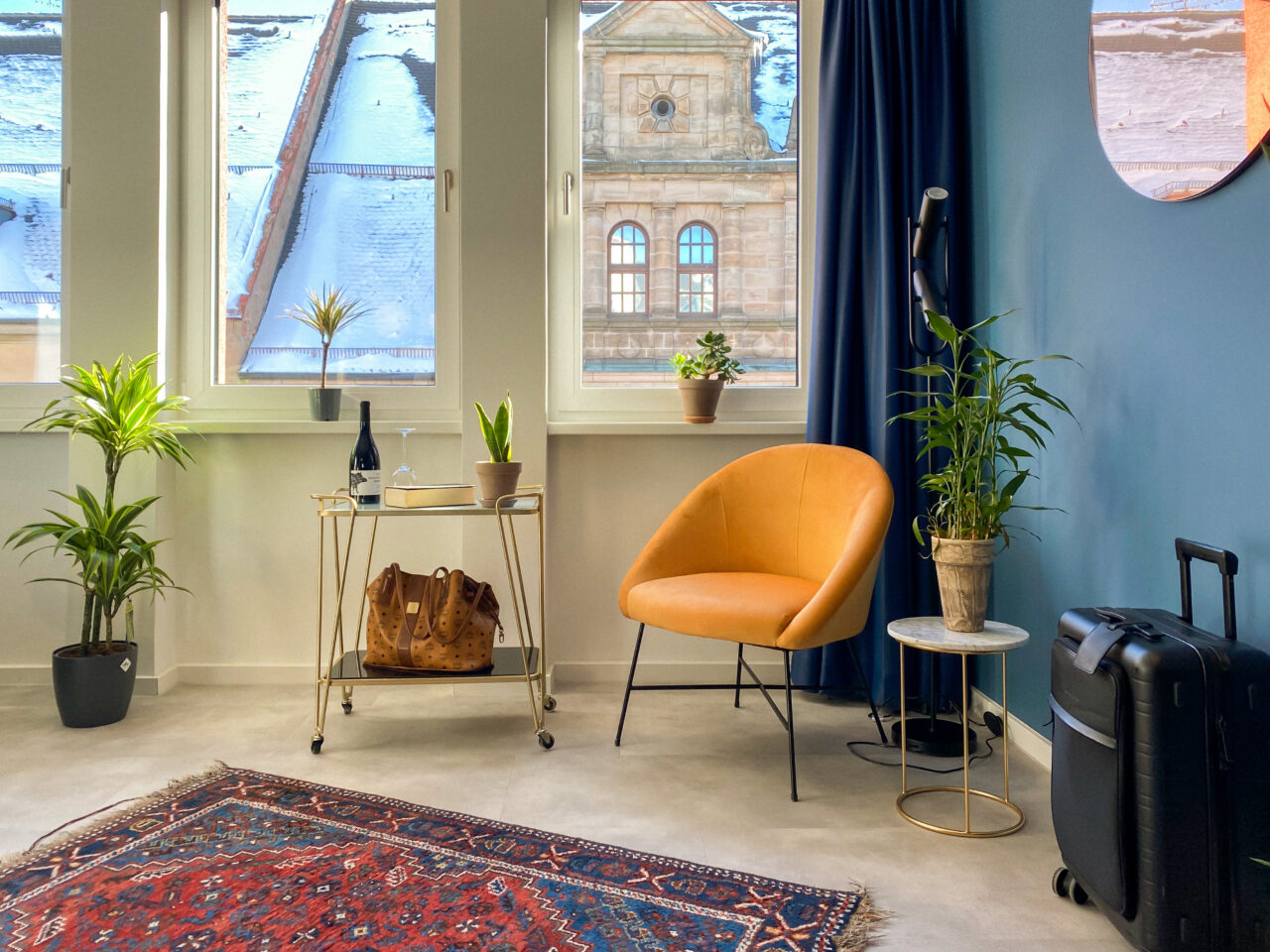 Senfgelber Sessel vor einer blauen Wand, davor ein gemusterter Teppich